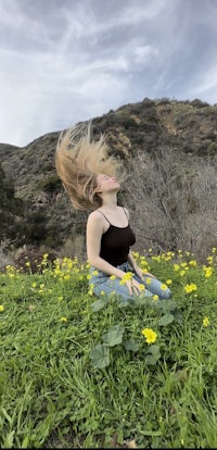 a woman sitting in a field with her hair blowing in the wind